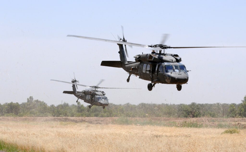 Two military helicopters land in a field.