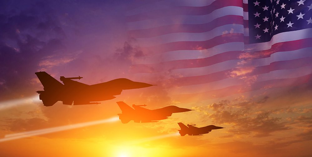 Three aircraft fighter jets flying in a sunset sky with the American flag faded in the background.