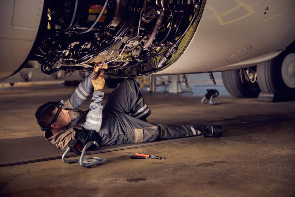 An aircraft mechanic on the ground is working on a plane's engine.