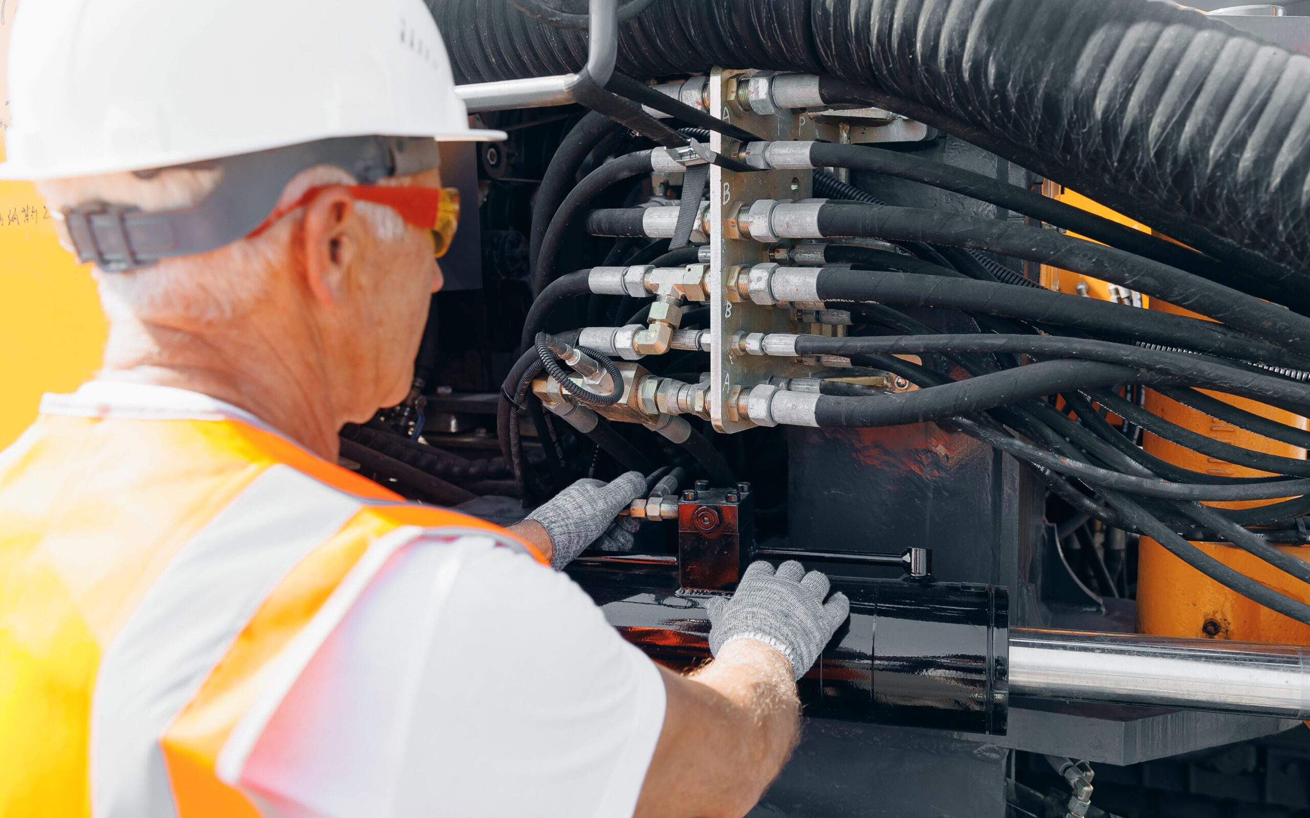 A man in a hardhat checks a hydraulic hose system.
