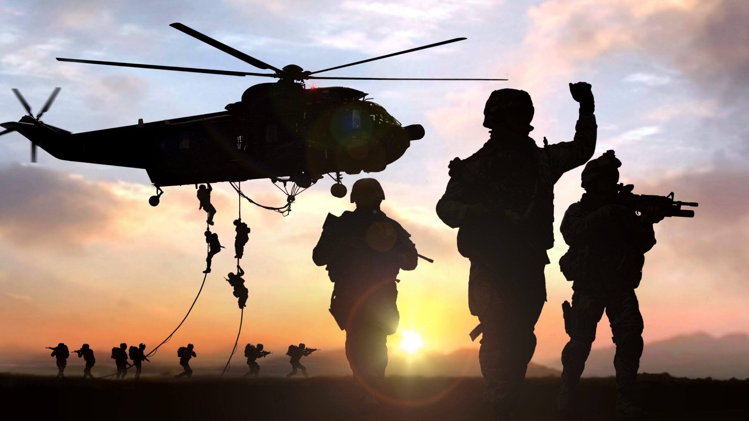 A military helicopter dropping off soldiers in a field.