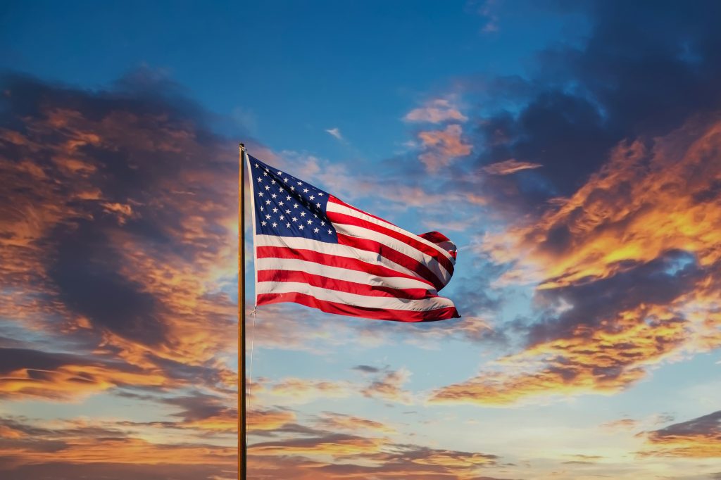 an American flag in the forefront of a sunset